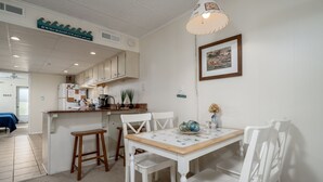 A clean, white interior with a kitchen area, wooden stools, and a dining table. - Experience your vacation in this spacious one bedroom condo with an ocean view. (Ocean City)
