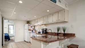 A kitchen with white cabinets, a granite countertop, and a sink. There is a coffee maker, a refrigerator, and a microwave. - Experience your vacation in this spacious one bedroom condo with an ocean view. (Ocean City)