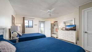 A hotel room with two beds, a ceiling fan, a dresser, a television, and a window with curtains. - Experience your vacation in this spacious one bedroom condo with an ocean view. (Ocean City)