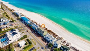 An aerial view of a coastal hotel with a long building along the beach, a parking lot, and a clear view of the ocean.