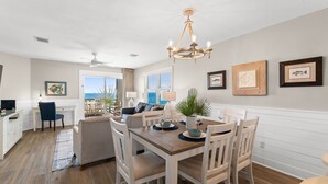 A dining area with a wooden table and white chairs, a chandelier, and framed artwork on the walls.