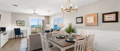 A dining area with a wooden table and white chairs, a chandelier, and framed artwork on the walls.