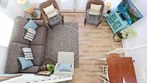 A modern living room with a grey sofa, two armchairs, a coffee table, a wooden dining table, and a large TV. - Pet Friendly - Steps From Beach - Narrow Escape (Cape San Blas)