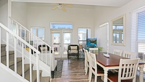 A dining area with a wooden table and white chairs, a ceiling fan, and a view of the beach through the door. - Pet Friendly - Steps From Beach - Narrow Escape (Cape San Blas)