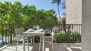 A balcony with a table set for dining, surrounded by lush greenery and a clear blue sky.