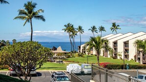 A resort with a view of the ocean, palm trees, and a parking area with covered cars.