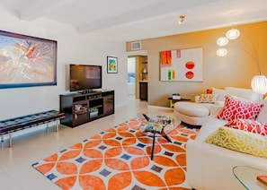A modern living room with a flat-screen TV, a sofa, a coffee table, and a patterned rug.