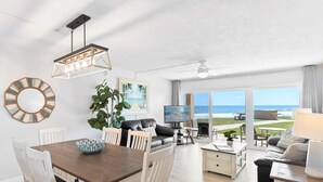 Amplia sala de estar con mesa de comedor, asientos, televisor y vista al océano.