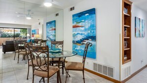 A dining area with a glass table, metal chairs, and a wooden bookshelf.