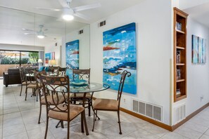 A dining area with a glass table, metal chairs, and a wooden bookshelf.