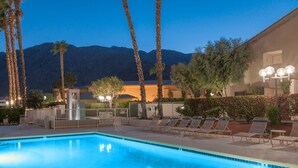 A swimming pool with lounge chairs, palm trees, and a mountain in the background.