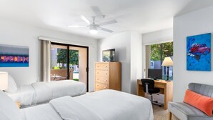 A hotel room with two beds, a desk, a chair, a sofa, a ceiling fan, and artwork on the walls.