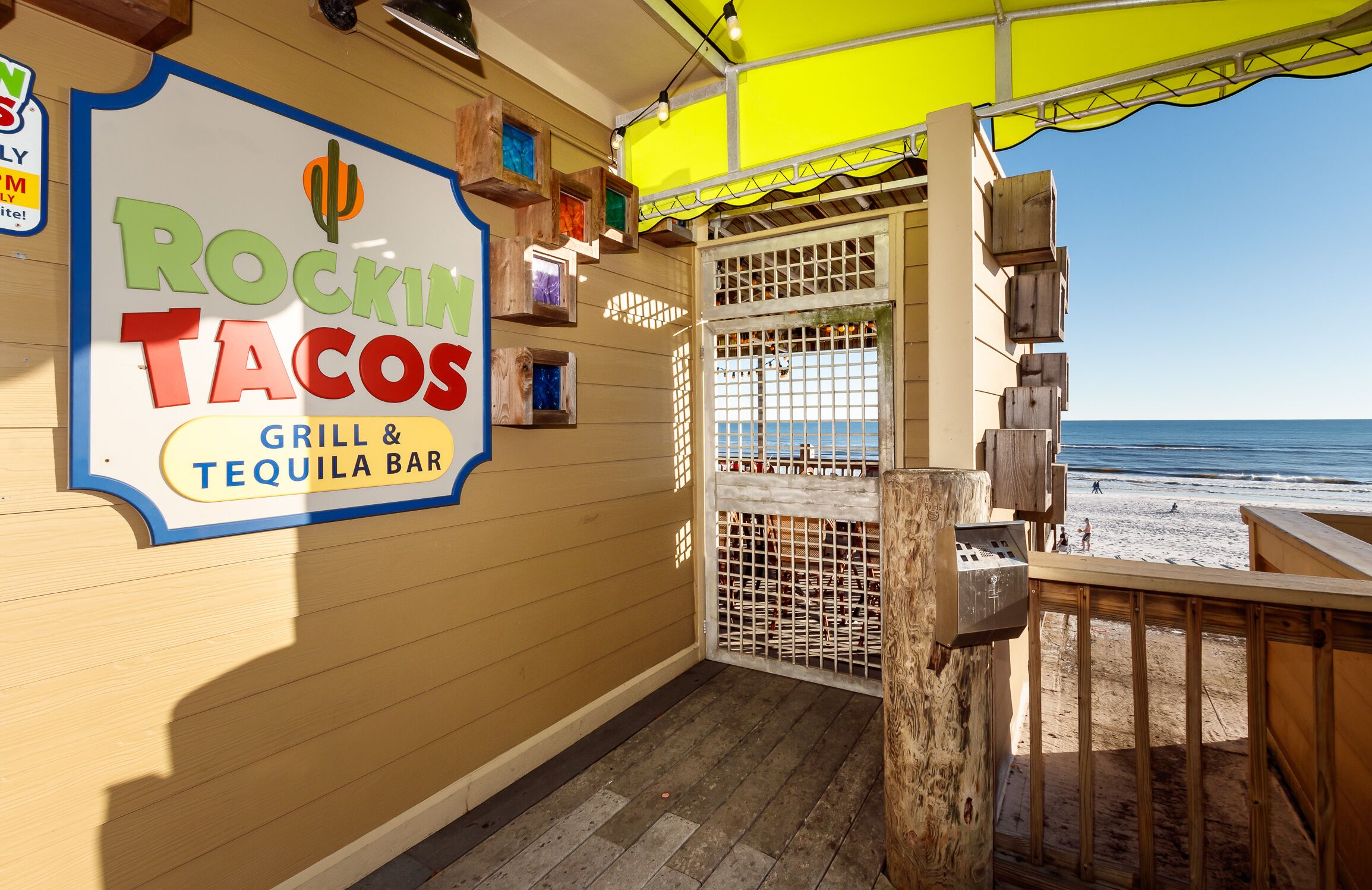En restaurang vid stranden som heter ”Rockin Tacos”, med en skylt, ett trädäck och utsikt över stranden.