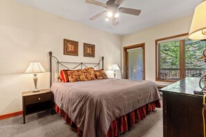 A bedroom with a bed, two bedside tables, a desk, a ceiling fan, and a window with a view.