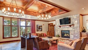 A spacious living room with a stone fireplace, wooden ceiling beams, and a large TV mounted on the wall. - Ski-in/ski-out, Hot tubs and sauna, Fireplace, Sleeps 8! (Breckenridge)