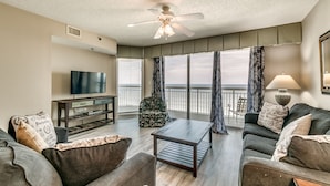 A living room with a television, a coffee table, a sofa, and a balcony with curtains.