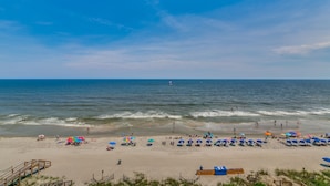 A beach with multiple umbrellas, a wooden walkway, and a view of the ocean.