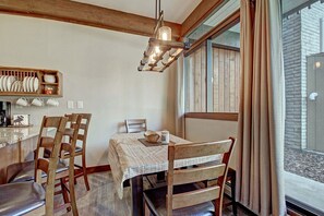 Un coin repas avec des chaises en bois, une table recouverte d’une nappe blanche et un luminaire suspendu.