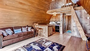 A cozy cabin interior with a wooden ceiling, a brown leather sofa, a wooden dining table with chairs, and a kitchen area. - Secluded & Cozy Antimony Cabin w/ Fire Pit (Antimony)