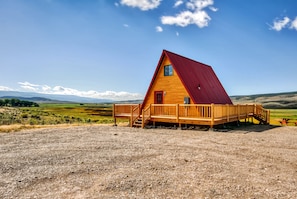 Eine Holzhütte mit rotem Dach, einer Holzterrasse und Blick auf die umliegende Landschaft.