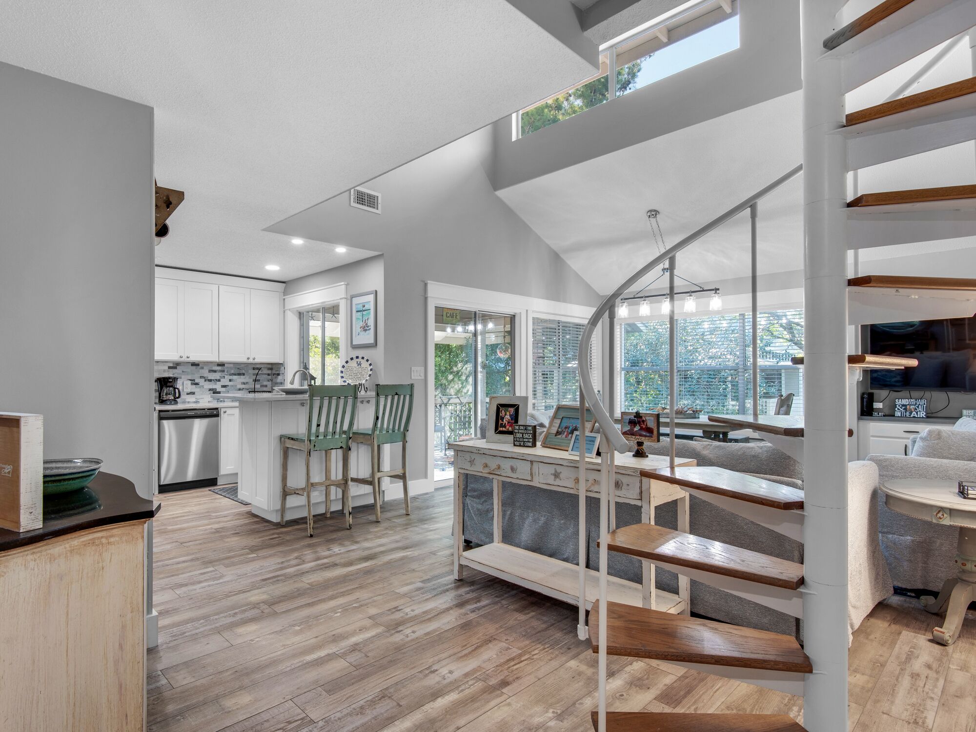 Eine moderne Küche mit weißen Schränken, ein Essbereich mit Holzsesseln und eine Treppe, die zu einem Wohnbereich mit Fernseher und Sitzgelegenheiten führt.
