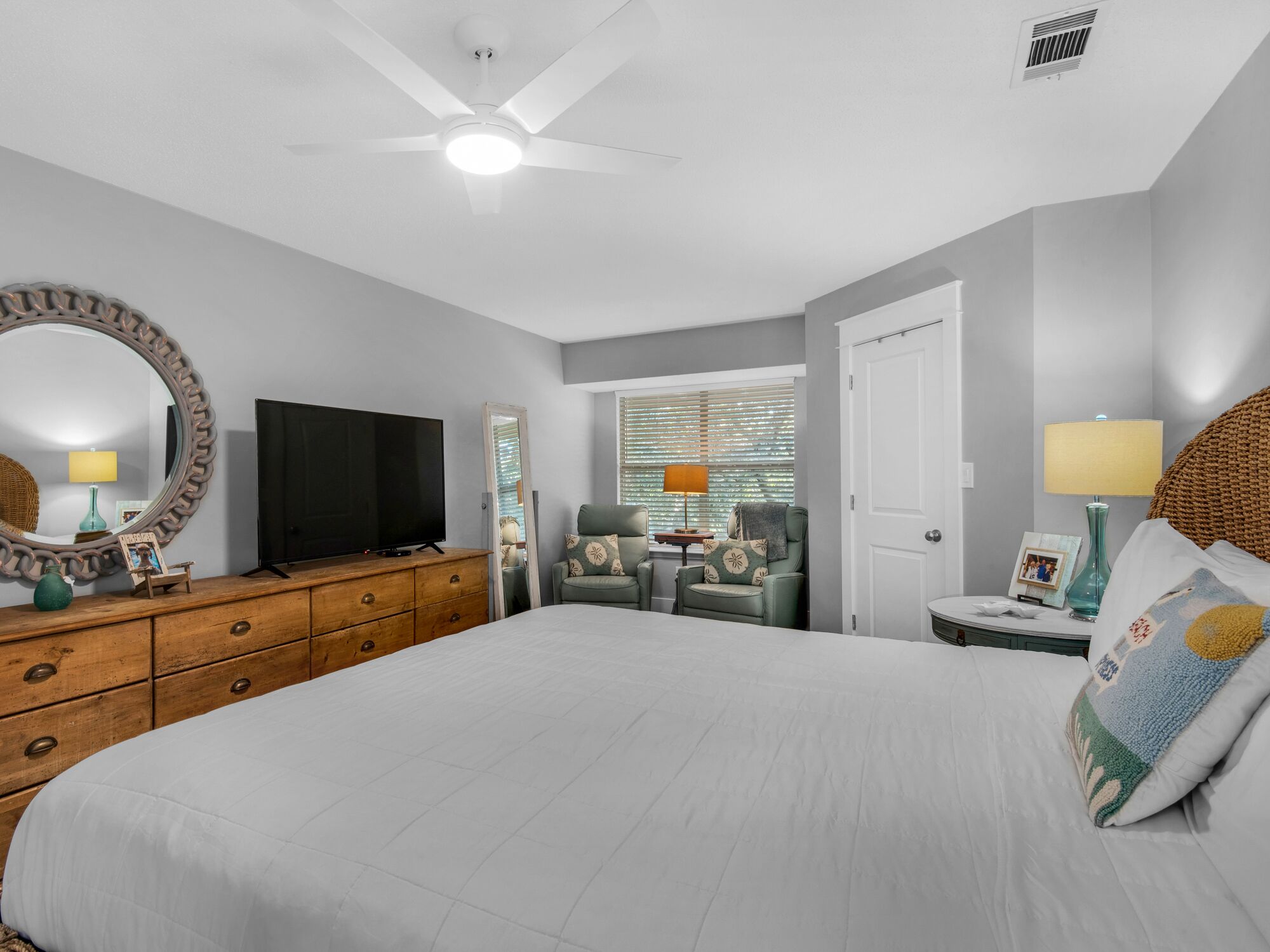 A bedroom with a large bed, a television on a dresser, a ceiling fan, and a window with blinds.