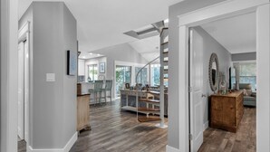 Een ruime woonkamer met een trap naar een hoger niveau, een keuken met moderne apparatuur, en een eetgedeelte met houten meubels.