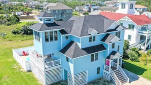 A multi-story house with a prominent tower, a covered porch, and a staircase leading to the upper levels. - The Life of Riley - NH MP 10.5, Ocean View, 265 Yds to Beach, Pool, Hot Tub, Pool Table, Flex Stays (Nags Head)