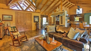 A spacious living room with a high ceiling, wooden beams, a leather sofa, a rocking chair, and a dining area with wooden furniture. - Beaver Creek Lodge: Stargazing Destination (Huntington)