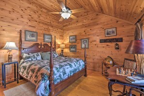 Une chambre à coucher aux murs lambrissés, dotée d’un lit à baldaquin, d’un ventilateur de plafond et d’un bureau en bois sur lequel sont disposées des pièces d’échecs.