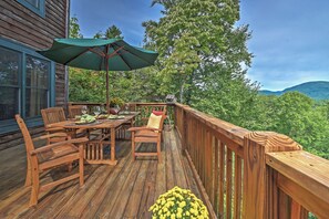 Une terrasse en bois avec une table et des chaises, un parasol et une vue sur la forêt.