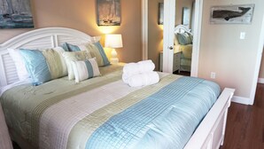 Una cama bien hecha con cabecera blanca, varios almohadones y una toalla doblada.