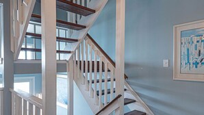 Eine hölzerne Treppe mit weißen Geländern führt zu einem Schlafzimmer mit einem Bett und einem Fenster.