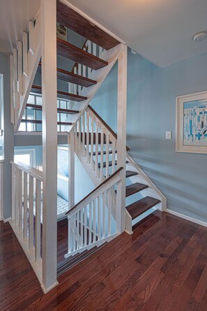 A wooden staircase with white railings leading to a bedroom with a bed and a window.