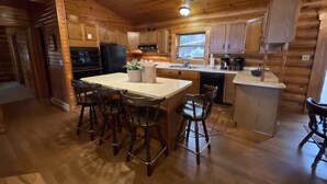 A wooden cabin-style kitchen with a central island, bar stools, and a large window.