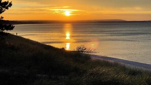 A sunset over a calm body of water with a grassy shoreline and distant land.