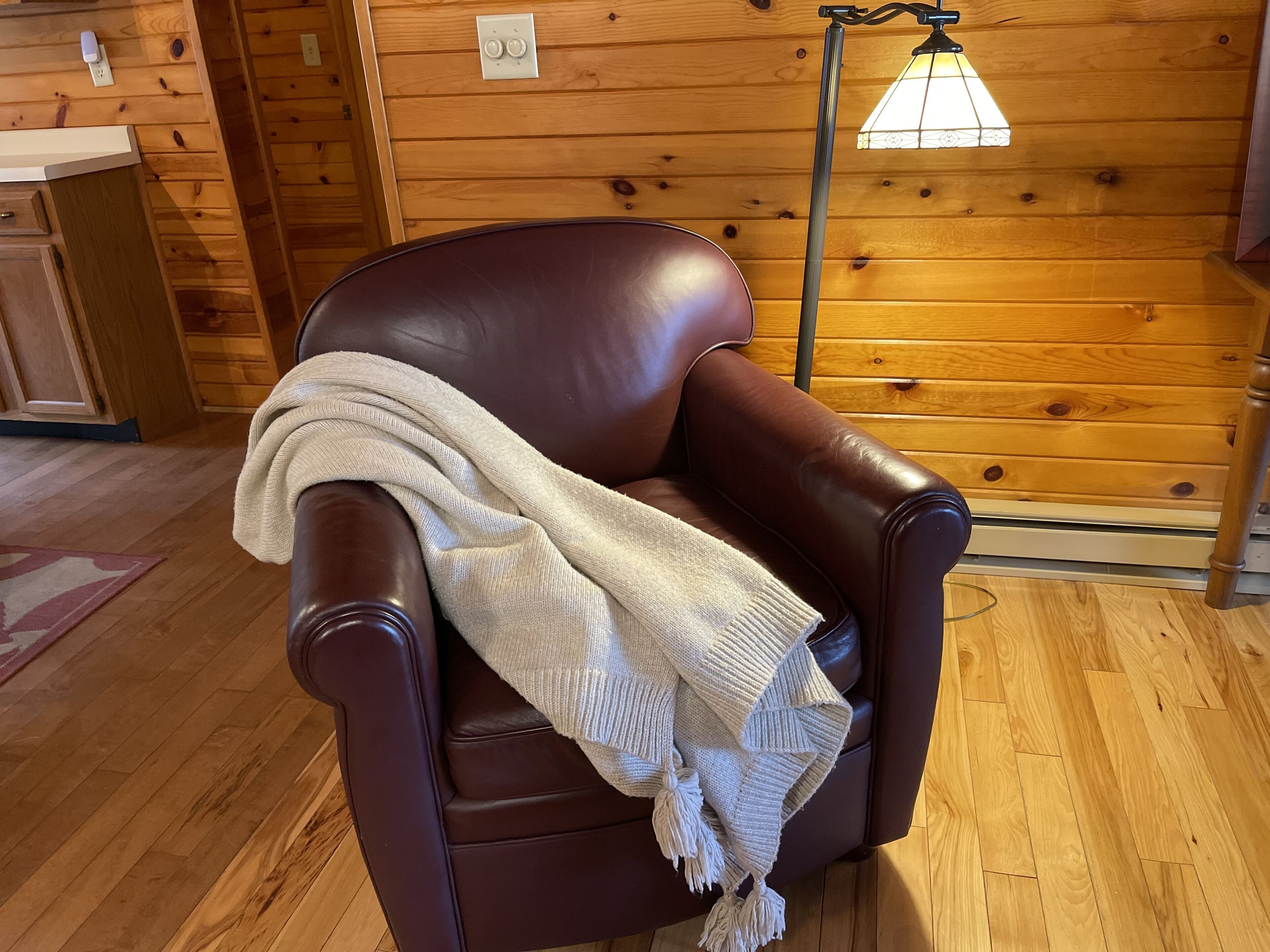 Un sillón de cuero marrón con un chal tejido blanco en el interior de una cabaña de madera.