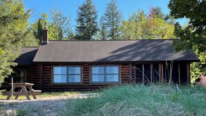 A log cabin with a chimney, two windows, and a picnic table.