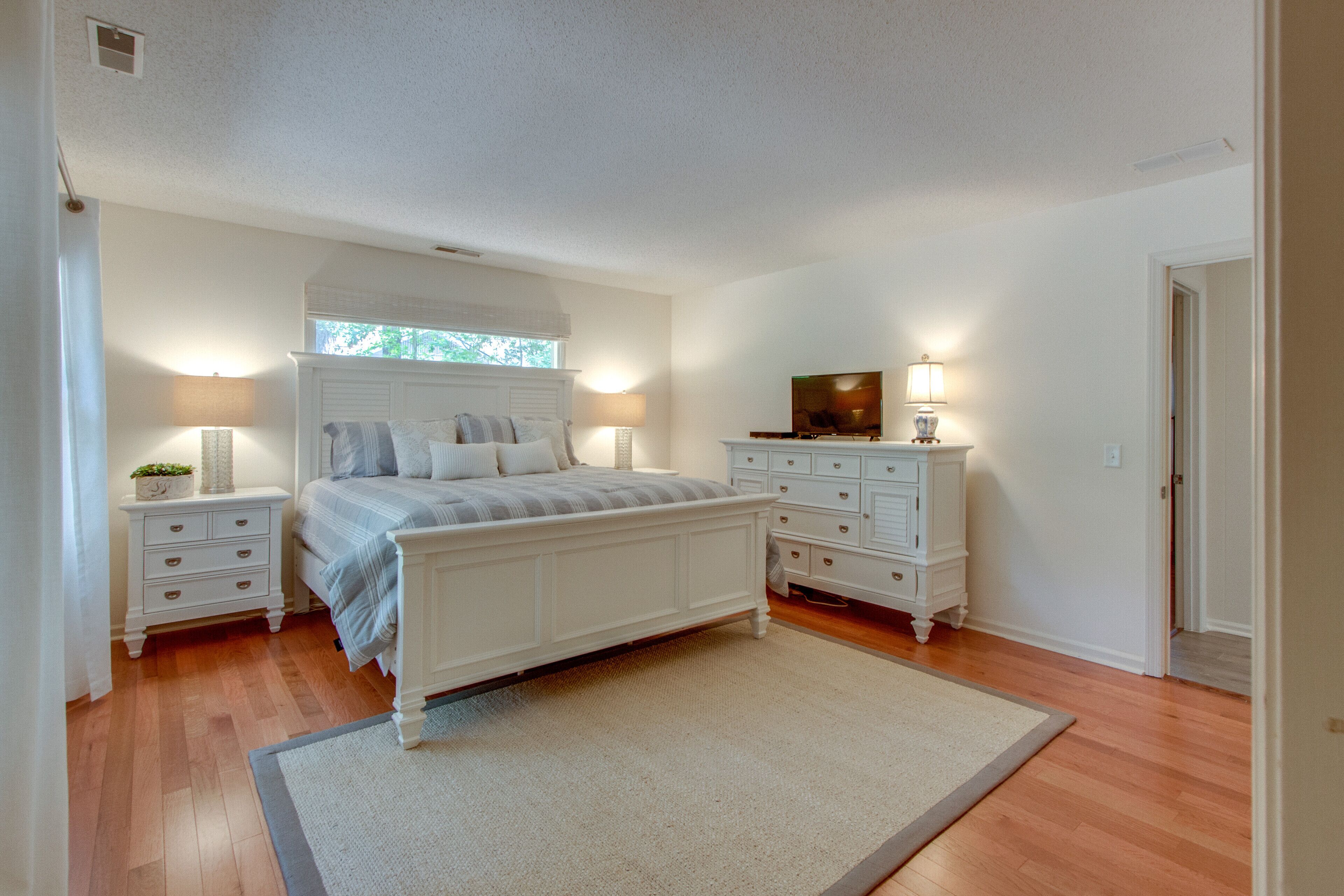 A bedroom with a bed, nightstands, a dresser, and a television.