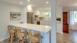 A kitchen with white cabinets, a stainless steel refrigerator, and a bar area with wicker chairs. - 20 Tupelo: Charming Sea Pines Home, Private Pool, Free Bikes (Hilton Head Island)