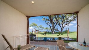 An outdoor seating area with lounge chairs and a table, overlooking a lawn with trees and a view of the ocean. - Aloha Aku Bamboo Suite – Discover Beachfront Serenity (Kihei)