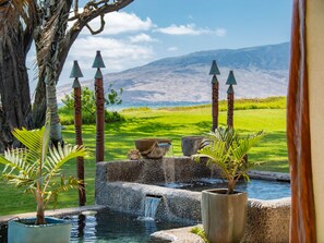 Tranquila zona de piscina al aire libre con cascada, rodeada de exuberante vegetación y vistas a montañas lejanas.