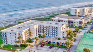 Um hotel à beira-mar com vários andares, estacionamento e quadra de tênis.