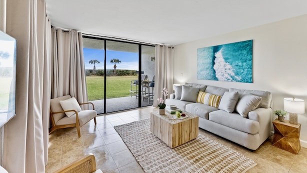 Uma sala de estar moderna com sofá, mesa de centro e uma janela grande com cortinas.
