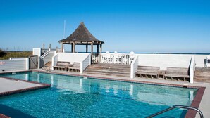 Un ciel d’un bleu éclatant, une piscine avec une terrasse en bois et un belvédère.