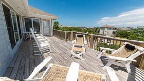 Une terrasse en bois avec des chaises longues blanches et une porte vitrée donnant sur un espace abrité.