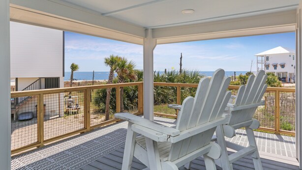 Un espacio al aire libre cubierto con dos sillas Adirondack blancas, una terraza de madera y vista al océano y la playa.