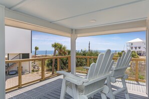 A covered outdoor area with two white Adirondack chairs, a wooden deck, and a view of the ocean and beach. - Single Level Home, Lots of Parking, Quiet Neighborhood ~ Brodie House (Indian Pass)