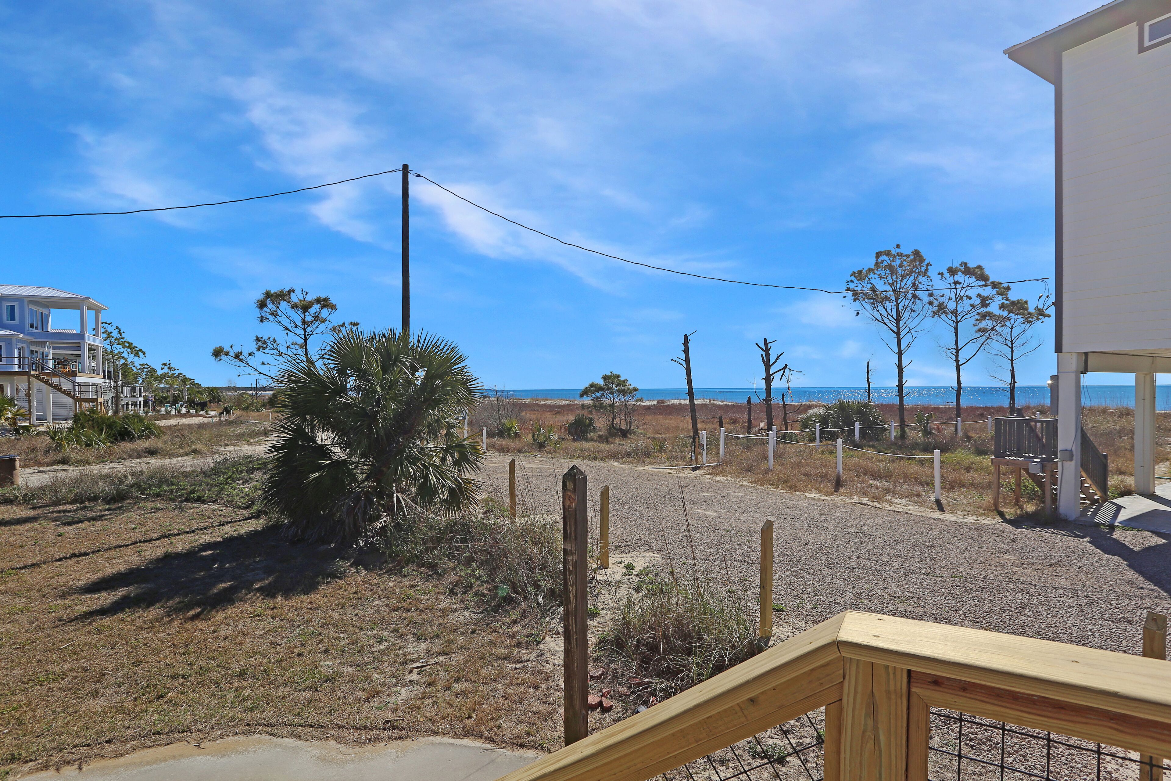 A residential area with a clear view of the ocean, a sandy path, and a wooden fence.