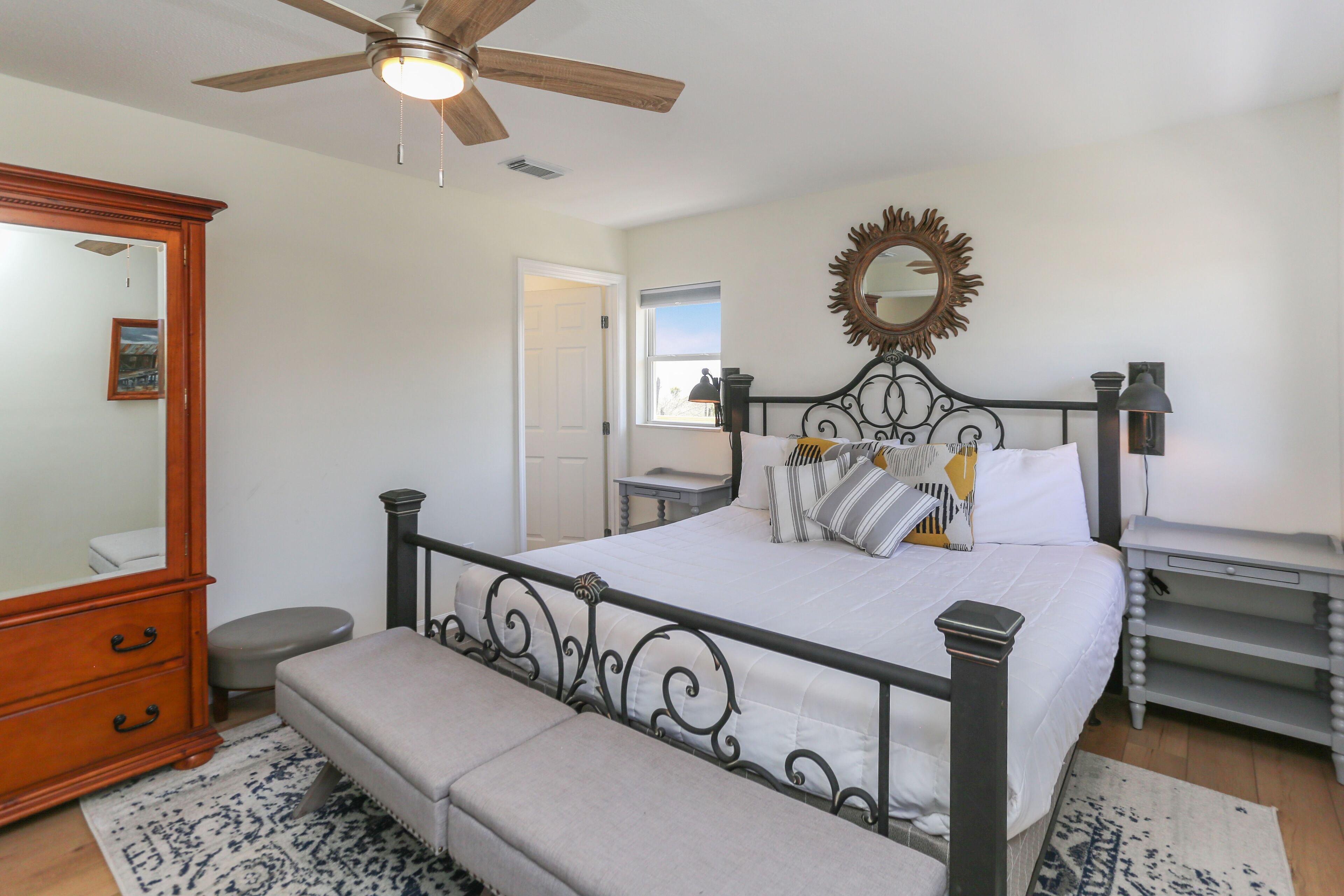 A bedroom with a bed, bench, dresser, and a ceiling fan.